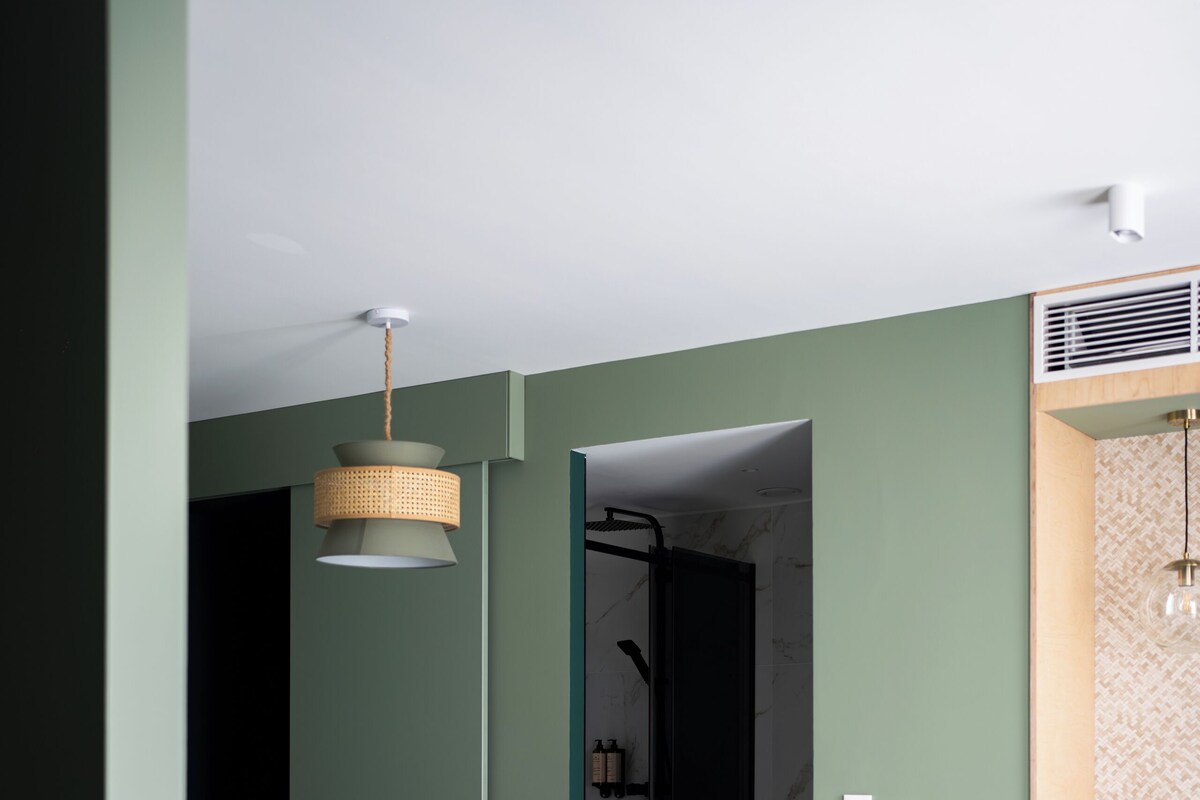 A bedroom with a bed, a hanging light fixture, a shower area, and a patterned rug.