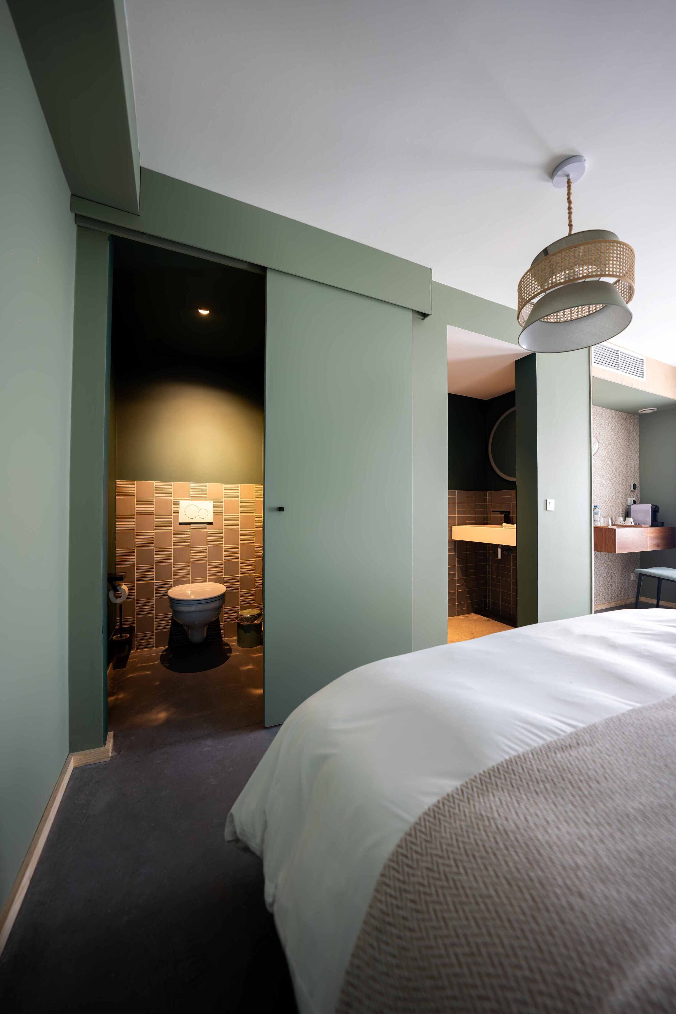 A hotel room with a bed, a bathroom with a toilet and sink, and a ceiling fan.