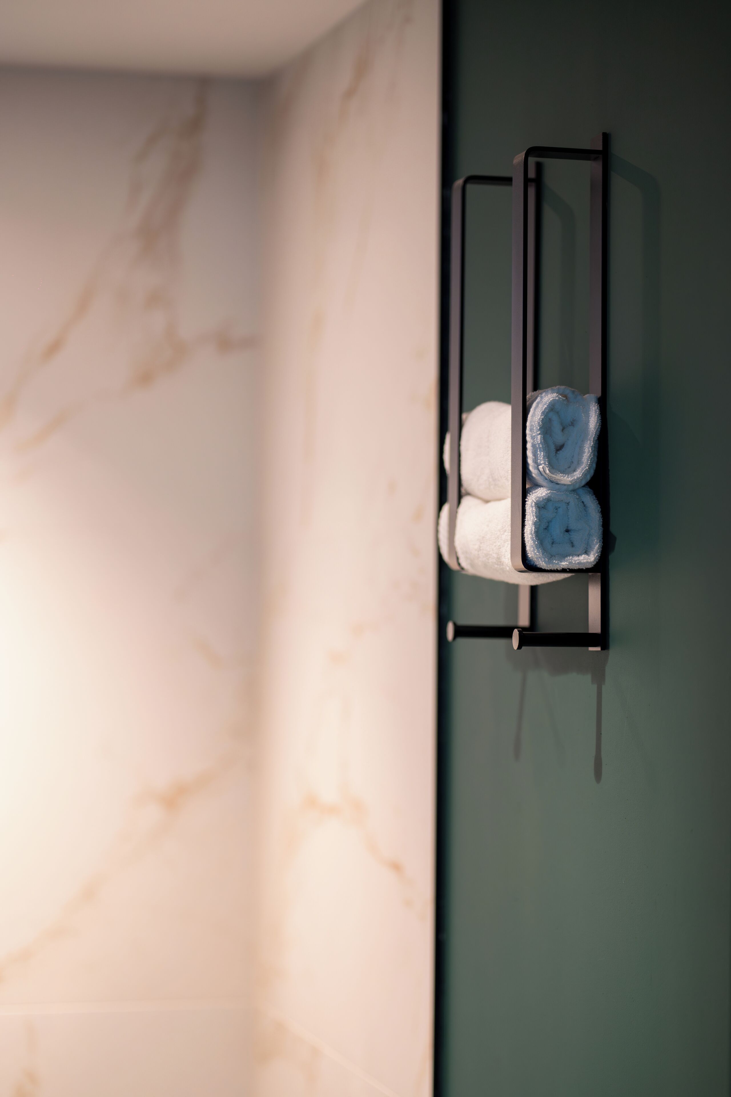 A bathroom with a marble wall and a towel rack holding two rolled towels.