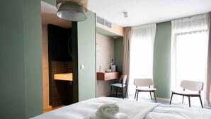 A hotel room with a bed, two chairs, a desk, and a bathroom.