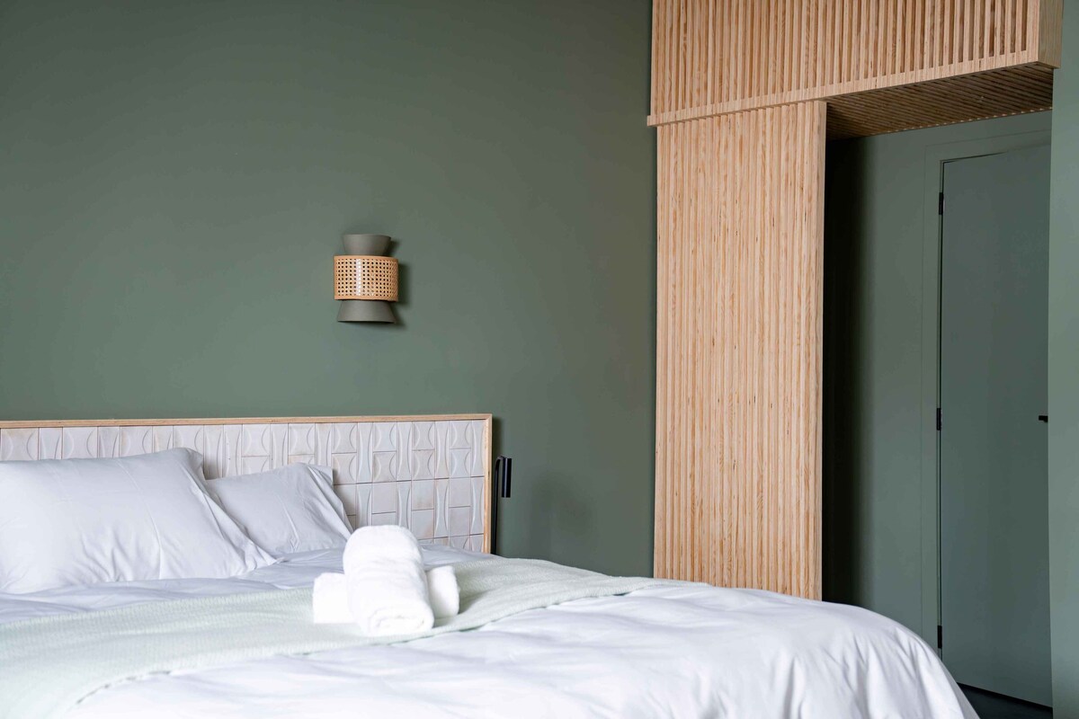 A neatly made bed with white linens, a headboard with a geometric pattern, and a wall-mounted light fixture.