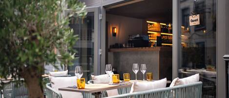 An outdoor dining area with wicker chairs and tables, a glass door entrance, and a sign reading "Owert".