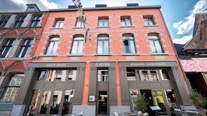 A hotel with a red facade, two ground-floor entrances, and outdoor seating.
