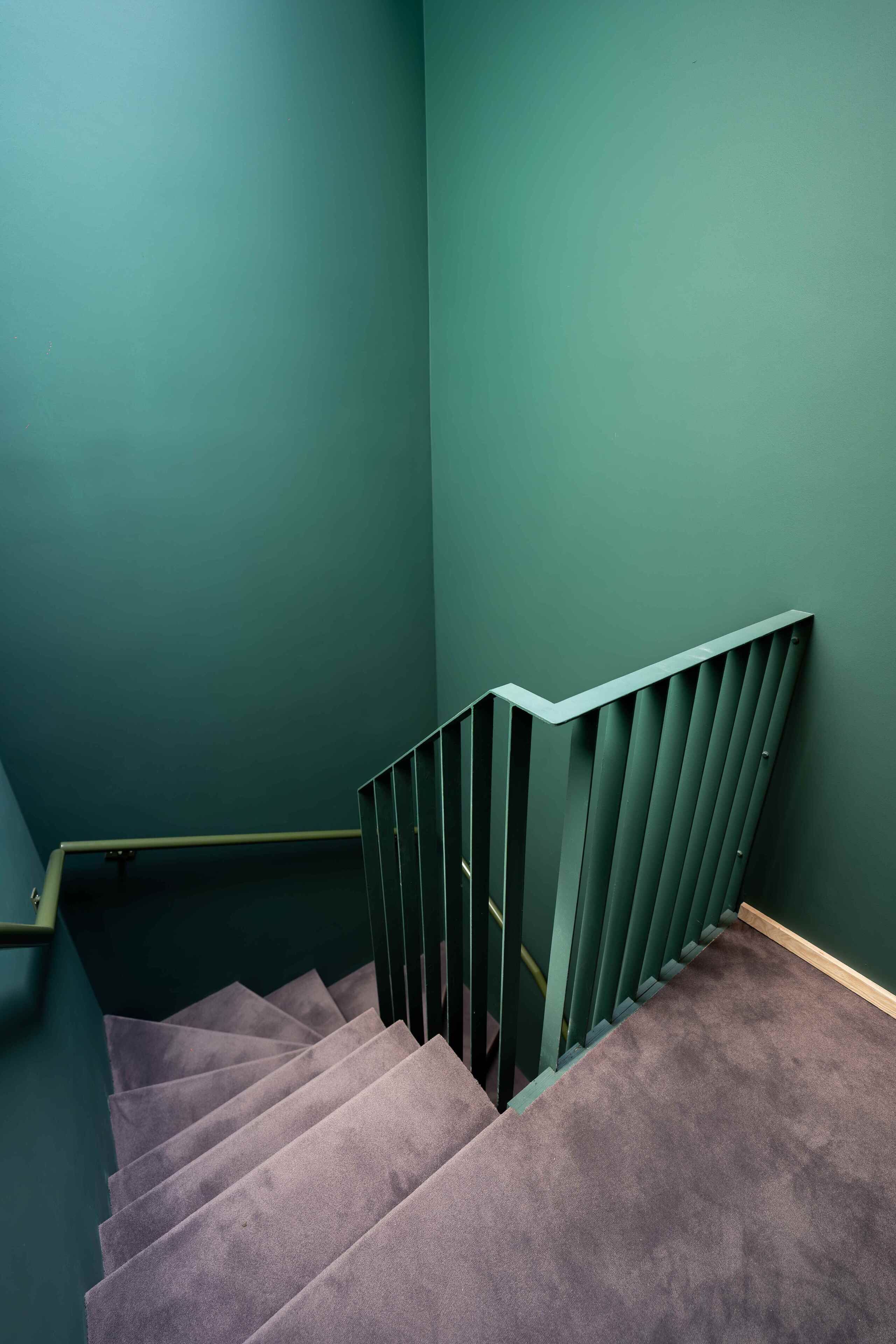 A staircase with a green wall and a grey carpet.