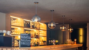 A bar area with a long counter, bar stools, and hanging pendant lights.