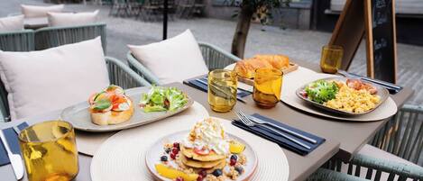 A table set with breakfast items including pancakes, croissants, and a salad, with a chalkboard menu in the background.