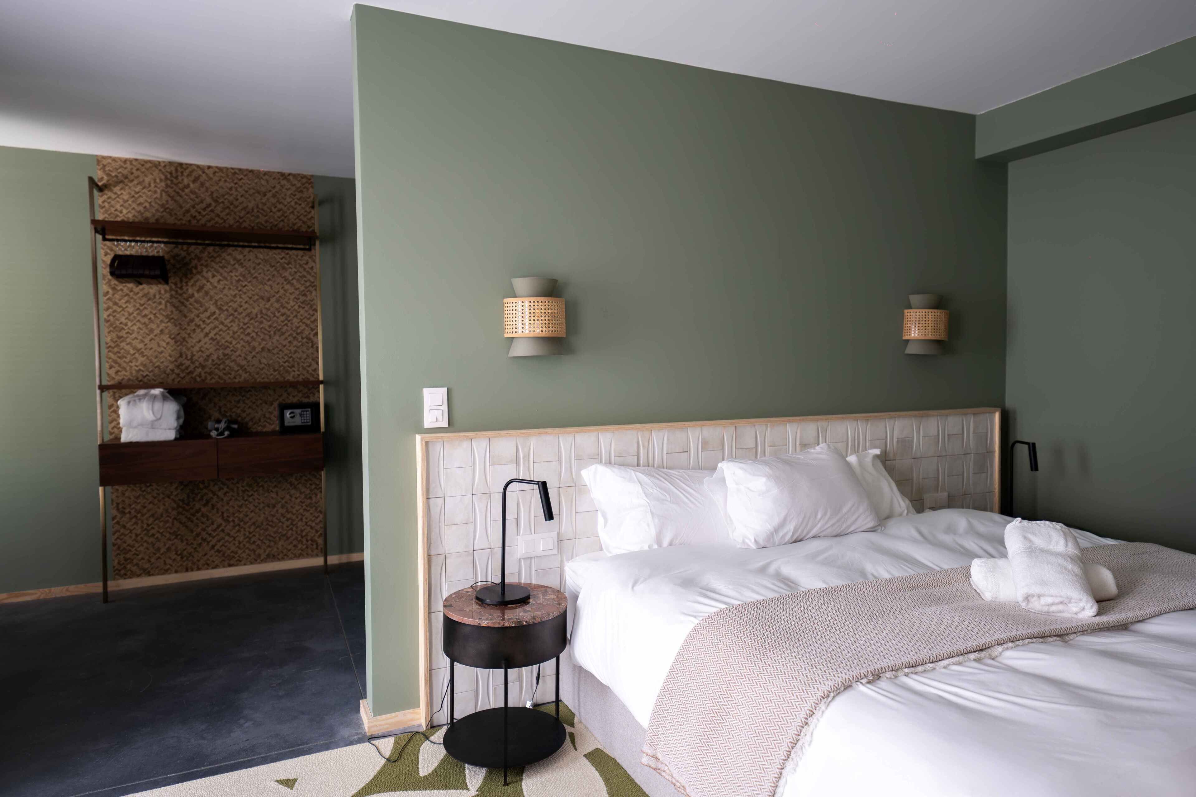A neatly made bed with white linens, a bedside table with a lamp, and two wall-mounted sconces.