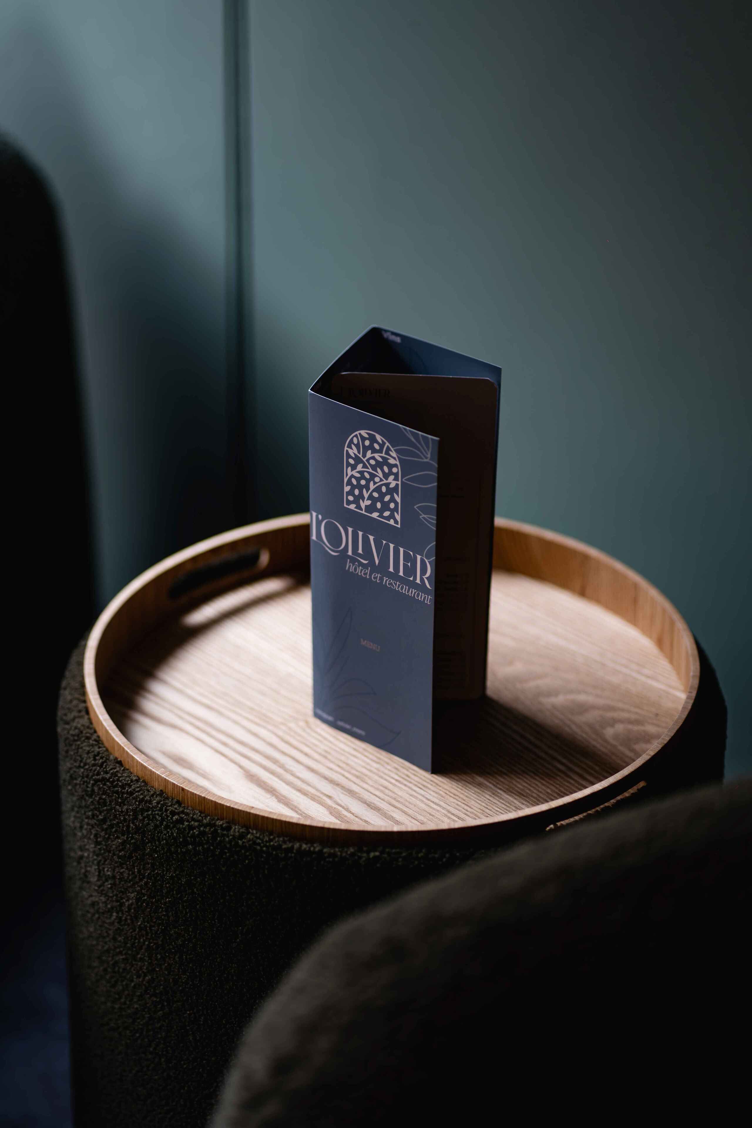 A dark blue booklet titled "L'IVRE HOTEL" on a wooden tray.