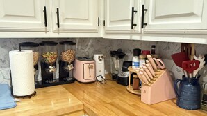 Uma cozinha com armários brancos, bancada de madeira, escorredor de louça, cafeteira, torradeira, liquidificador e porta-facas.