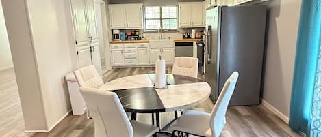 Una cocina moderna con armarios blancos, una mesa de comedor con cuatro sillas y un refrigerador grande.