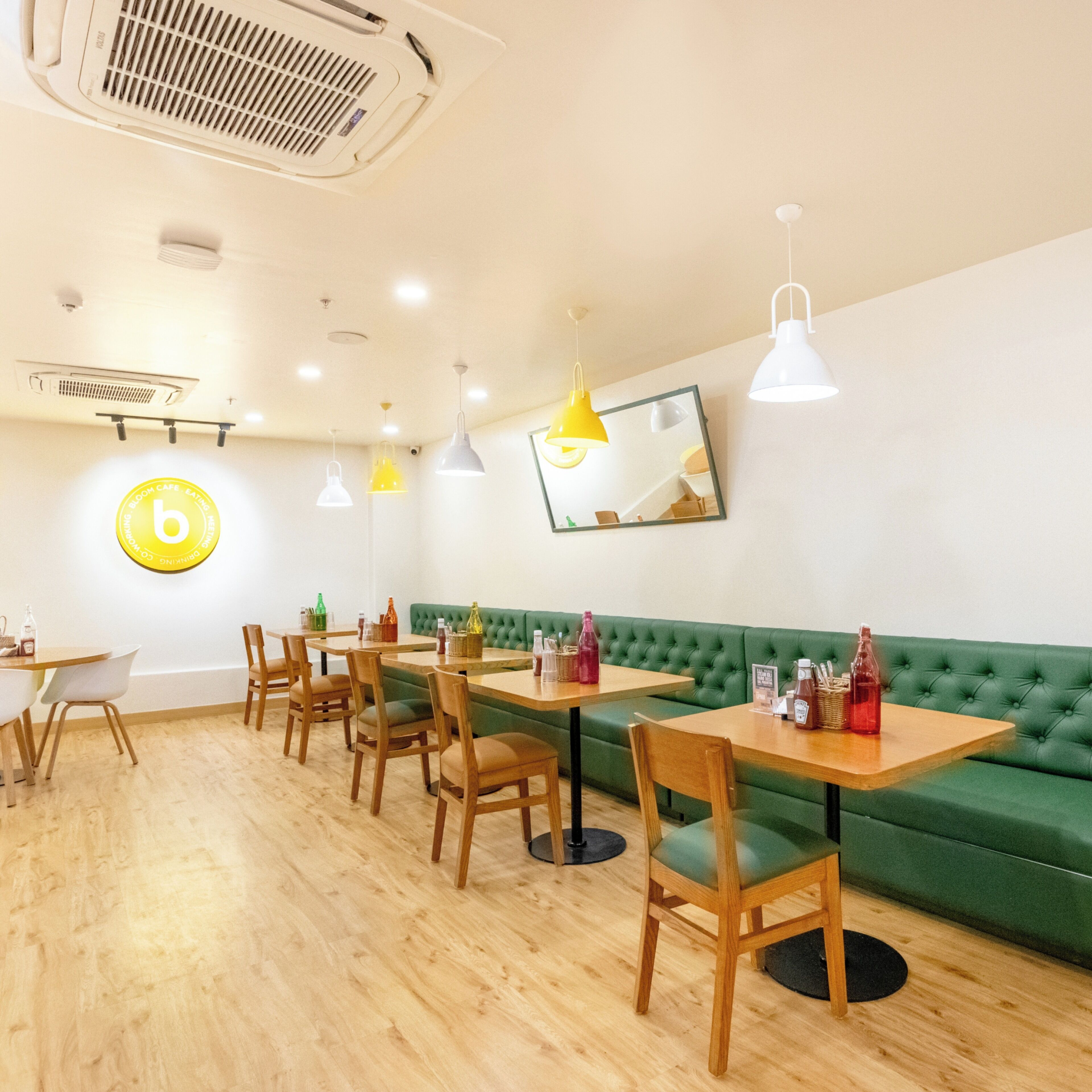 A restaurant interior with wooden tables and chairs, a green cushioned bench, and pendant lighting.