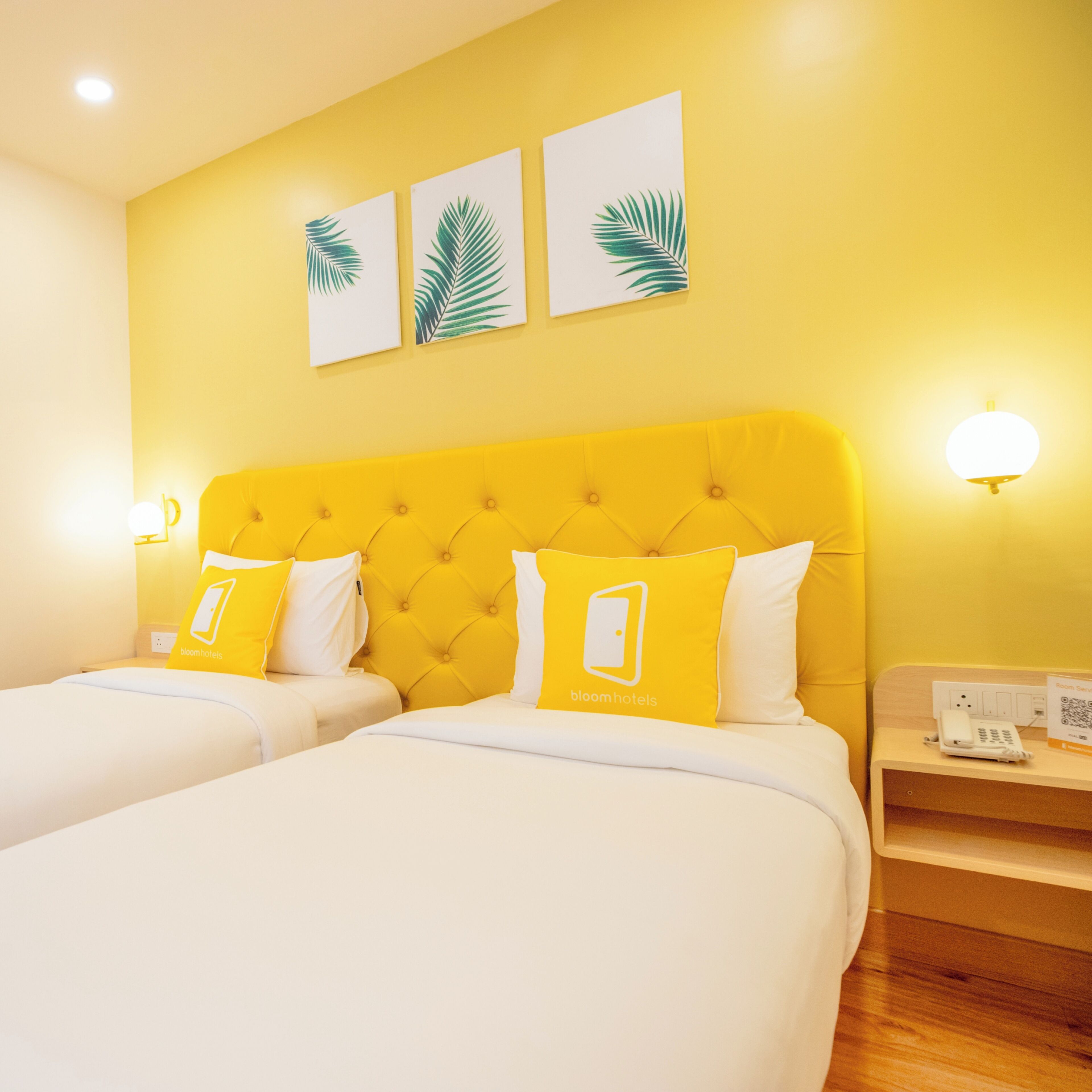 A hotel room with two beds, a yellow headboard, and three wall-mounted leaf paintings.