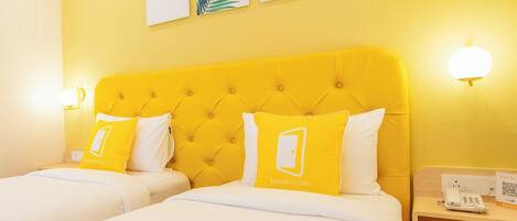A hotel room with two beds, a yellow headboard, and three wall-mounted leaf paintings.