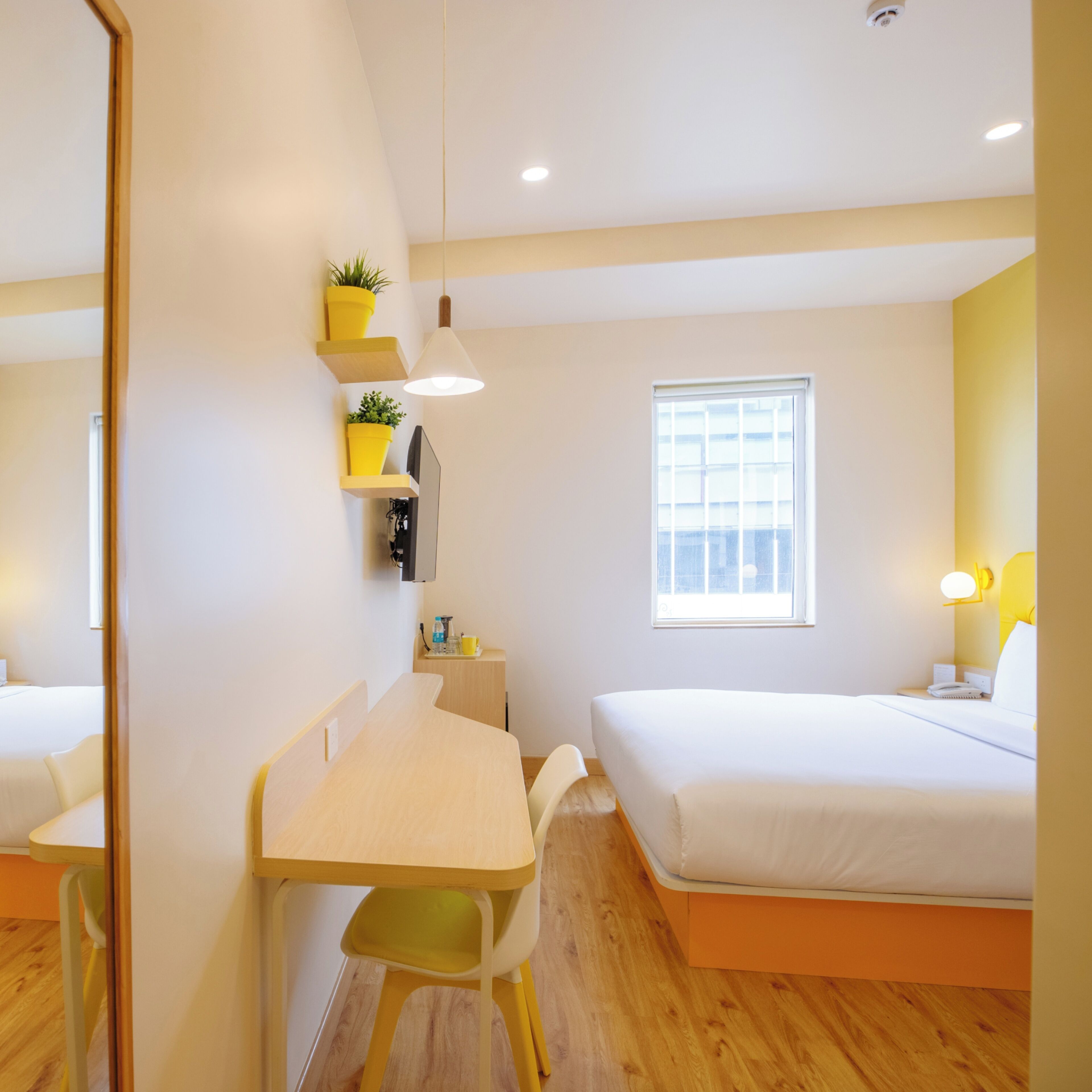 Ein modernes Hotelzimmer mit Schreibtisch, zwei Betten, einem Fenster und einem kleinen Tisch mit Stuhl.
