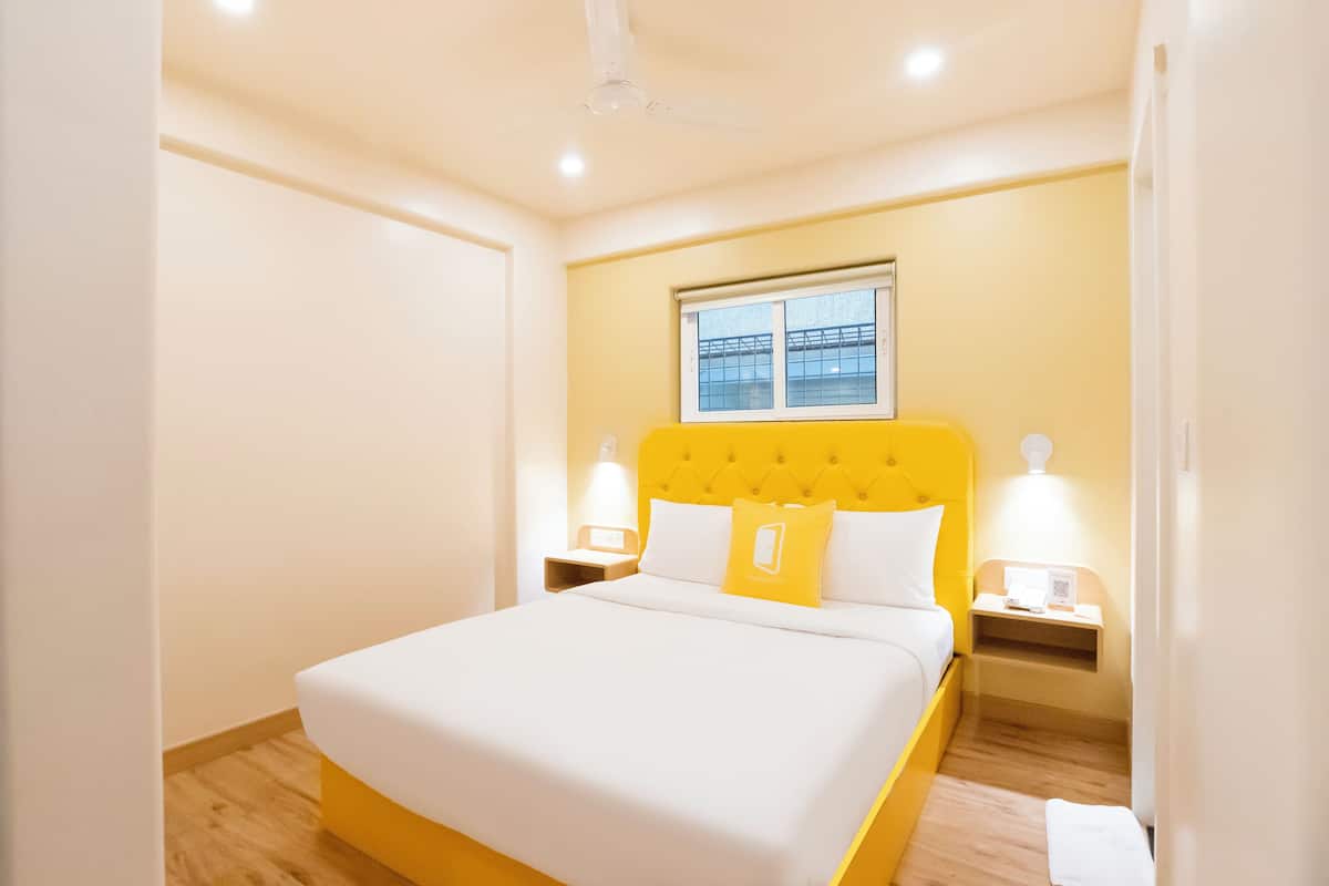 Quarto de hotel com uma cama, duas mesas de cabeceira, uma janela e um ventilador de teto.