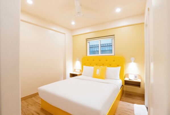 Una habitación de hotel con una cama, dos mesitas de noche, una ventana y un ventilador de techo.