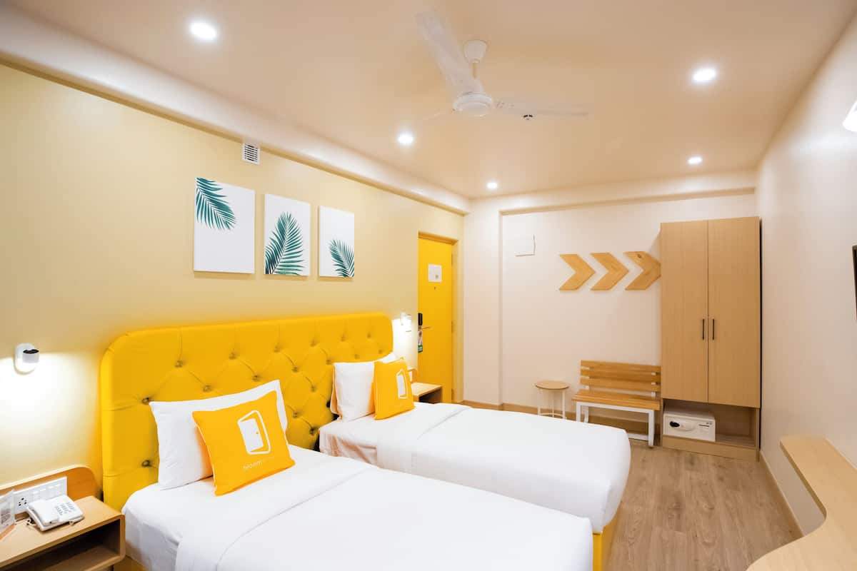 Quarto de hotel com duas camas, guarda-roupa de madeira, uma mesa pequena e um banco.