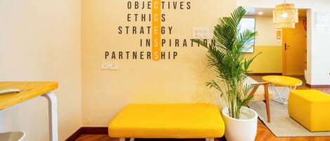 A room with a wooden floor, a yellow bench, a potted plant, and a wall with motivational words.