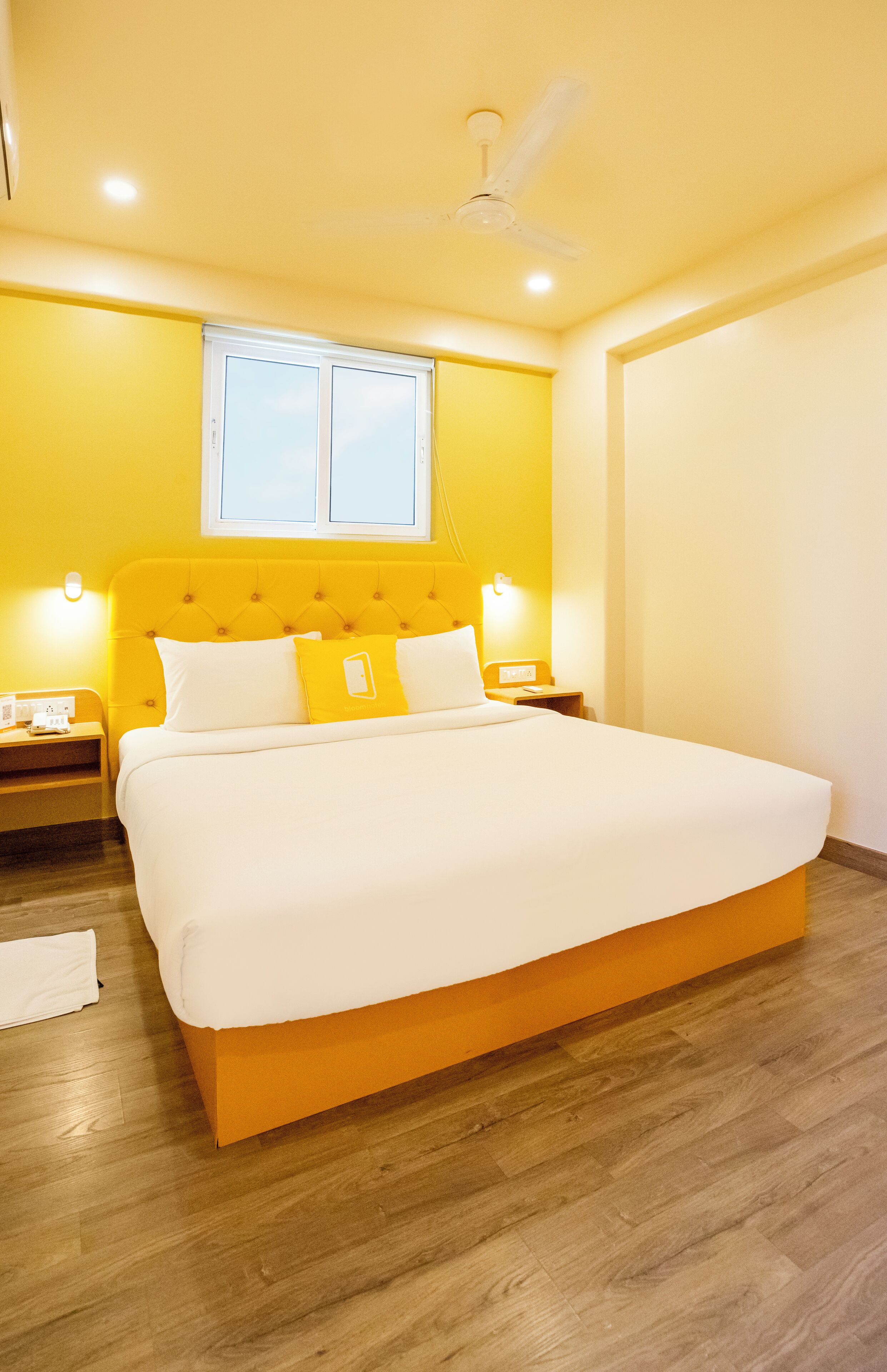 Una habitación de hotel con una cama grande, suelo de madera, ventilador de techo y una ventana con persianas.