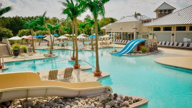 Un espace piscine aménagé dans un complexe hôtelier, avec un toboggan aquatique, des chaises longues et des palmiers.