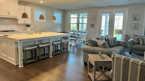 Une cuisine moderne avec des meubles blancs, un îlot central doté de tabourets et des luminaires suspendus.