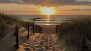 Un sentier de sable qui longe la plage et mène à l’océan, avec une clôture en bois de chaque côté.