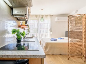 A compact hotel room with a kitchenette, a bed with a mosquito net, a potted plant, and a view of the outside. - Beach La Pineda by Interhome (La Pineda)