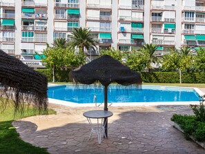A swimming pool with a thatched umbrella and a metal table, surrounded by hexagonal tiles and greenery. - Beach La Pineda by Interhome (La Pineda)