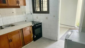 A kitchen with white tiled walls, wooden cabinets, a gas stove, and a window with bars.