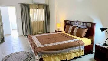 A bedroom with a bed, a nightstand, a lamp, a window with curtains, and an air conditioning unit.
