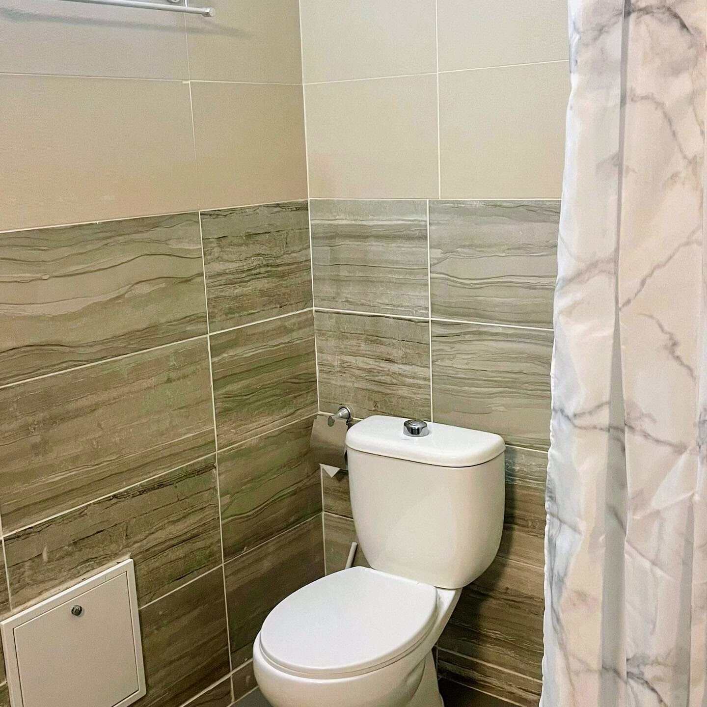 A bathroom with a toilet, a shower curtain, and tiled walls.