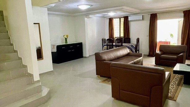 A spacious living area with a brown sofa set, a dining table with chairs, and a staircase leading to another level.