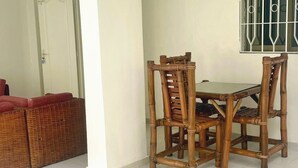 A dining area with a table and four chairs, a wicker sofa, and a window with bars.