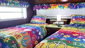 Een slaapkamer met twee bedden, elk overdekt met kleurrijke beddengoed met vrede-en-liefde symbolen.