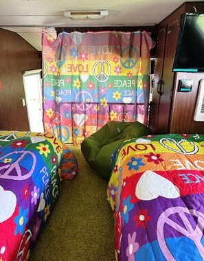 A room with two beds, a green bean bag, and a curtain with peace symbols and the word "LOVE".