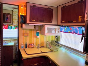 A compact kitchen with wooden cabinets, a microwave oven, a sink, and a window with blinds.