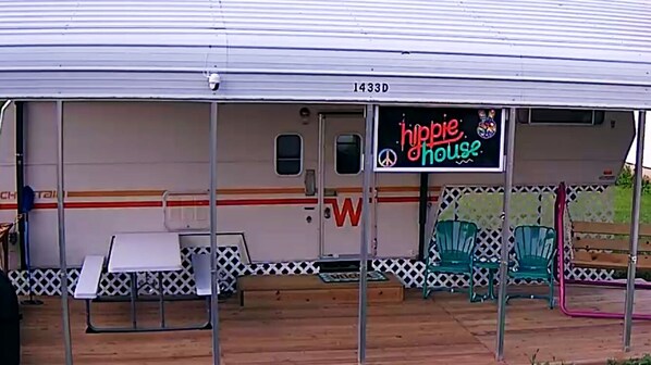 A mobile home with a 'hippie house' sign, a small porch area with chairs, and a table.