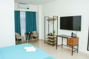 A hotel room with a bed, a desk, two chairs, a TV, and a window with curtains. - Amar Residences (Iligan)