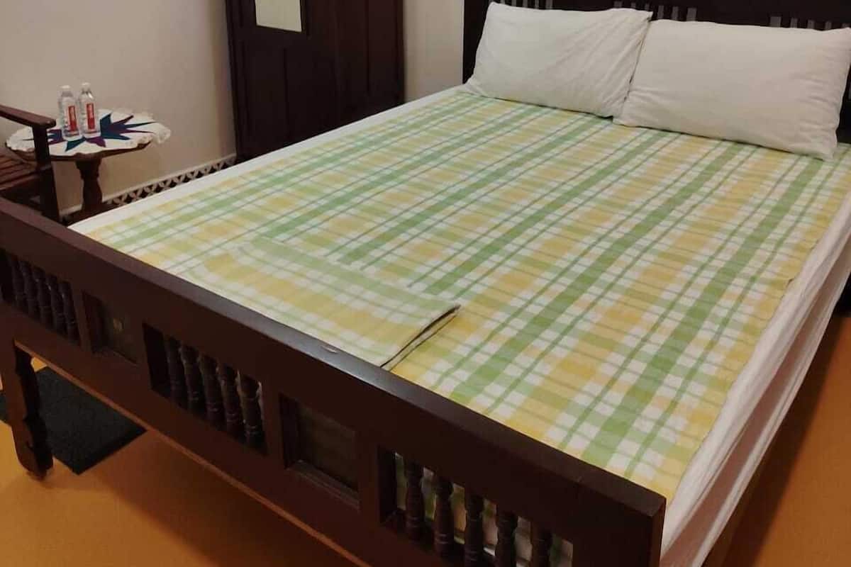 A single bed with a checkered bedspread, a wooden headboard, and a nightstand with water bottles.