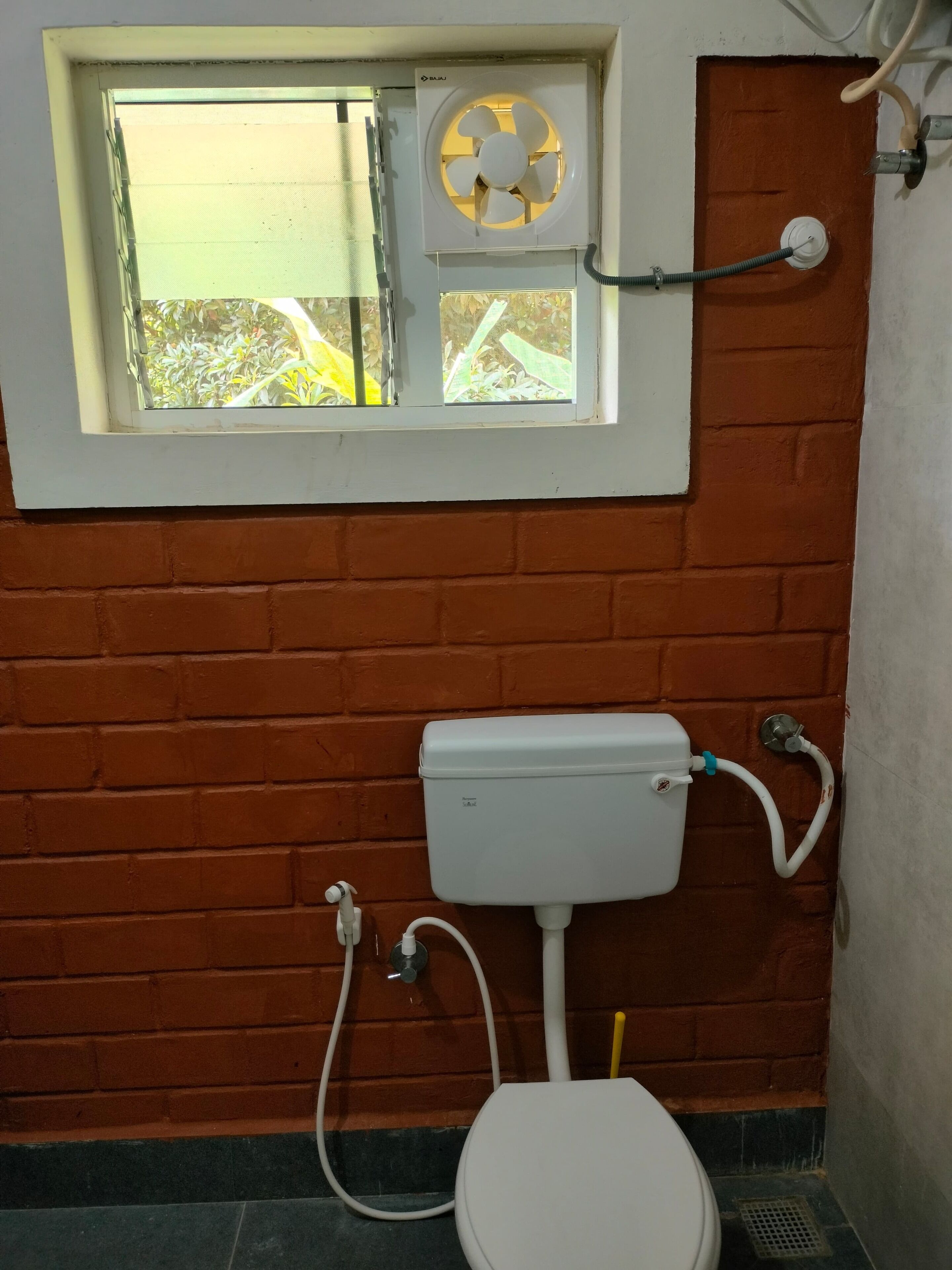 A bathroom with a window, a white toilet, and a fan.