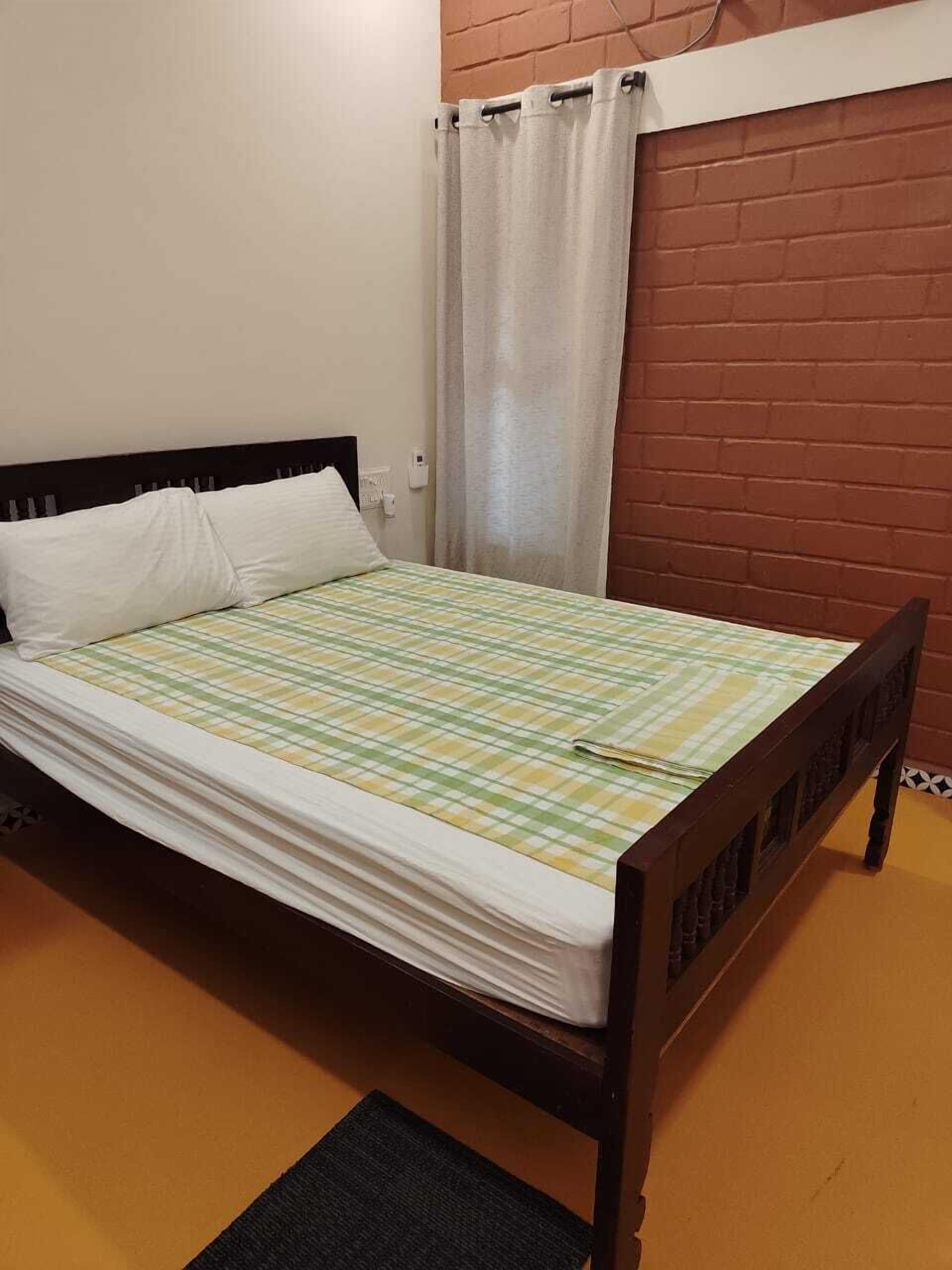 A single bed with a checkered bedspread, a white pillow, and a dark wooden headboard.