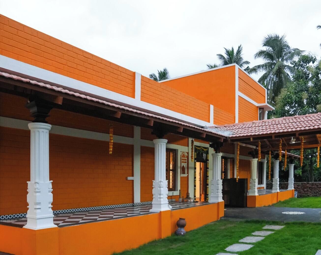 A two-story building with orange walls and white columns, featuring a covered porch with hanging decorations.