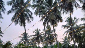 An outdoor dining area with a pool, surrounded by palm trees and string lights. - TRK Farms Vinmeen Retreat (Katpadi)