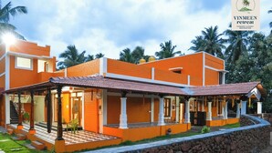 A modern two-story building with a flat roof, large windows, and a covered outdoor area with a stone wall. - TRK Farms Vinmeen Retreat (Katpadi)