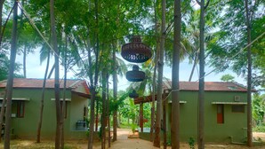 A pathway leading to a row of green-roofed buildings with a hanging lantern. - TRK Farms Vinmeen Retreat (Katpadi)
