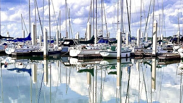 En lysthavn med flere sejlbåde i havnen, stille vand og træbrygger.