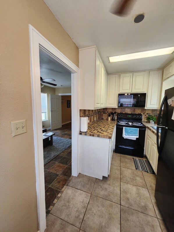 A kitchen with white cabinets, a black stove, a microwave, and a refrigerator.