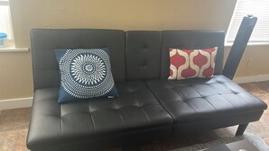 En sort lædersofa med to dekorative puder, et lille bord og et vindue med persienner.