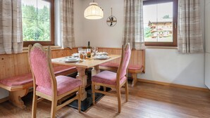 A dining area with wooden benches and a table set for four, large windows with curtains, and a hanging light fixture.