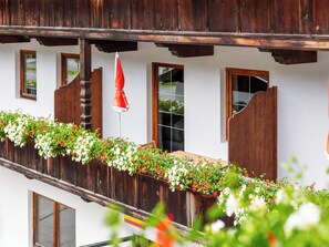 Un balcon traditionnel en bois, agrémenté de jardinières et d’un parasol rouge.